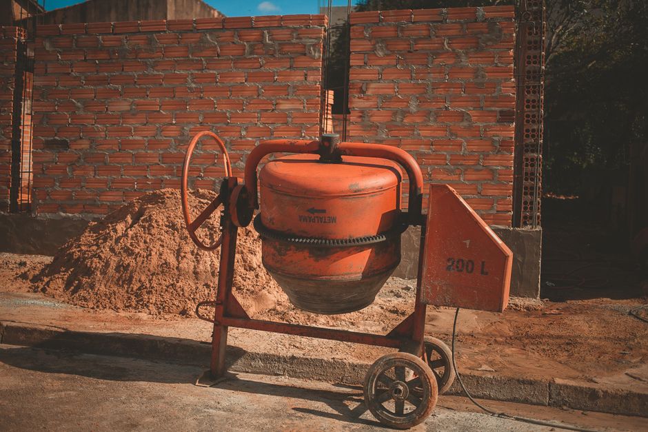 Orange cement mixer at a construction site with a brick wall background, under daylight.